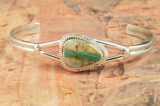 Genuine Boulder Turquoise set in Sterling Silver Bracelet. The cabochon is Boulder Turquoise, you can see the veins of Turquoise running through the host rock. The Boulder Turquoise Mine is located in northeast Nevada. It was discovered in 1970 by a Shoshone sheep herder. Production is small due to the remote location and winter weather. Boulder Turquoise is valued for both it's beauty and rarity. Every stone is unique. Created by Navajo Artist Lucy Valencia. Signed L. J. by the artist.